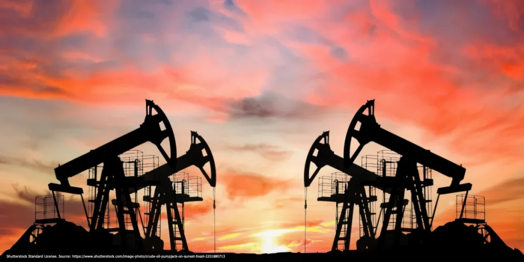 Oil pumpjacks silhouetted against a red-orange sunset sky.