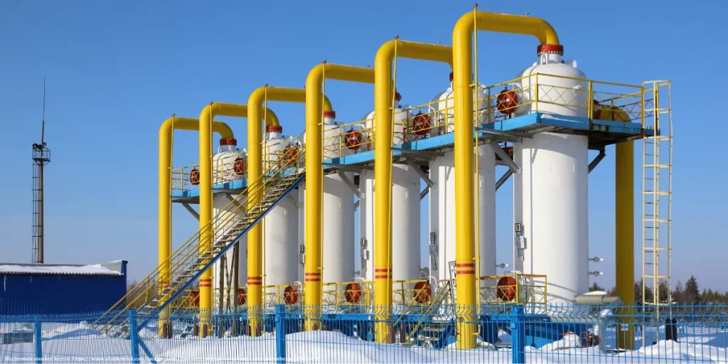 Gas transit infrastructure with yellow pipelines and white storage units at a snowy industrial facility.