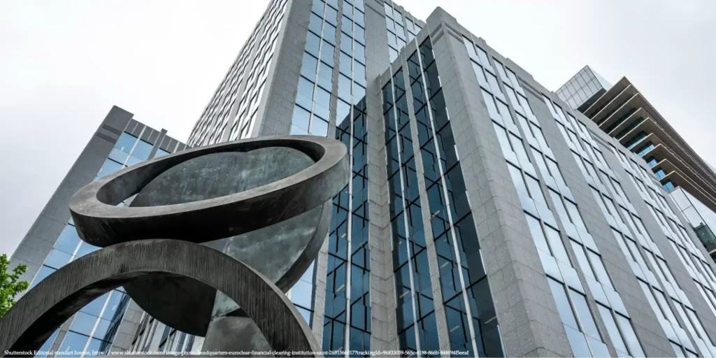 Modern glass office building with abstract metal sculpture in front, illustrating the interview with Benjamin Hilgenstock and his commentary on EU Loan Plan.