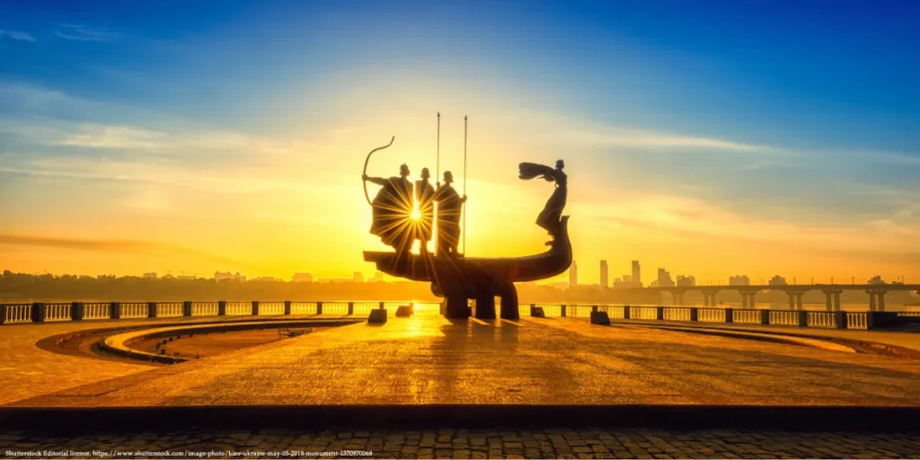 Monument to Kyiv’s founders silhouetted at sunrise over the Dnipro River.