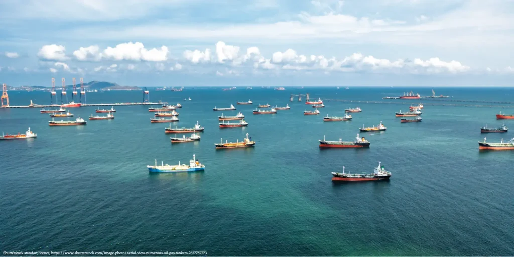Oil tankers anchored across blue coastal waters near a port.
